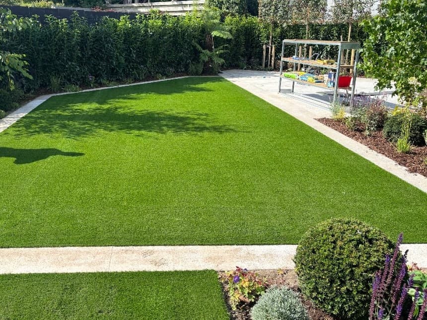 Artificial grass lawn framed by pale paving strips and planted borders
