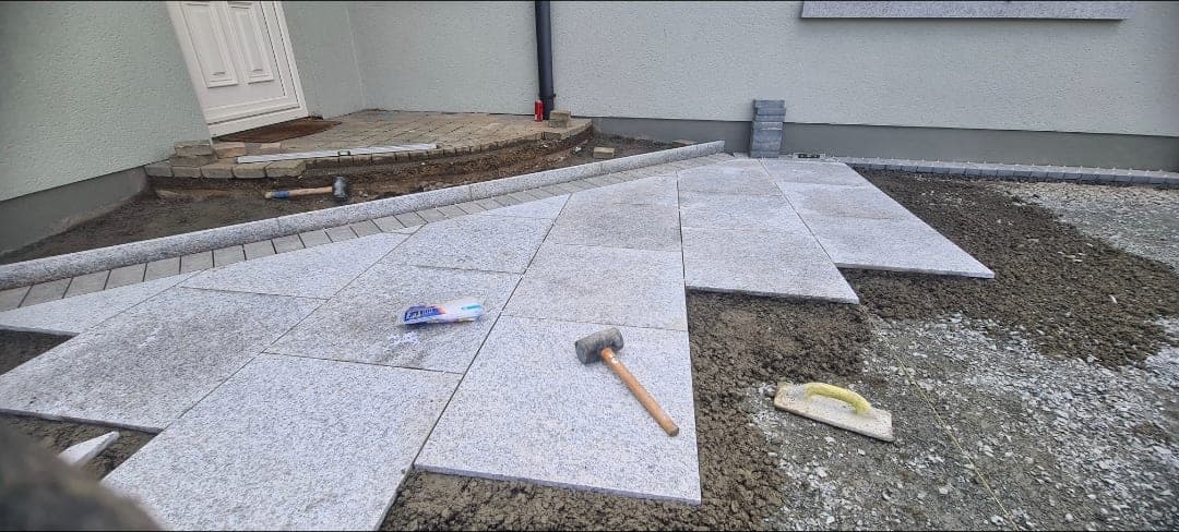 Granite patio slabs being laid to line and level beside a house entrance, with mallet and float on the surface