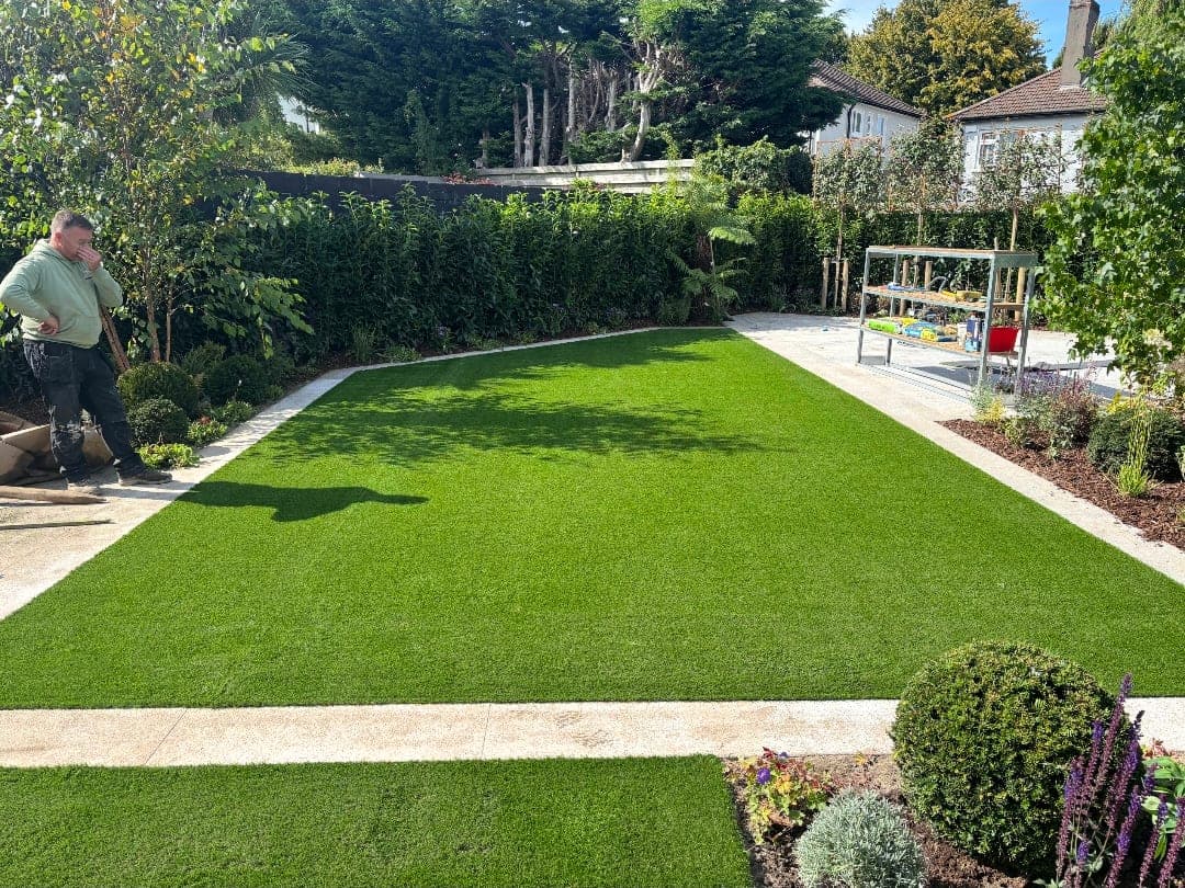 Rear garden artificial lawn framed by granite paving strips and mature planting