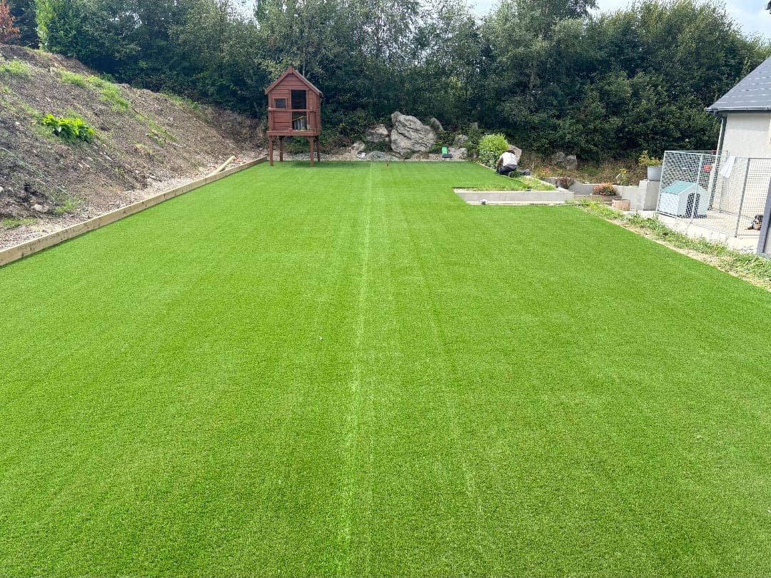 Long artificial grass lawn running to a raised timber playhouse, edged with a concrete retaining kerb