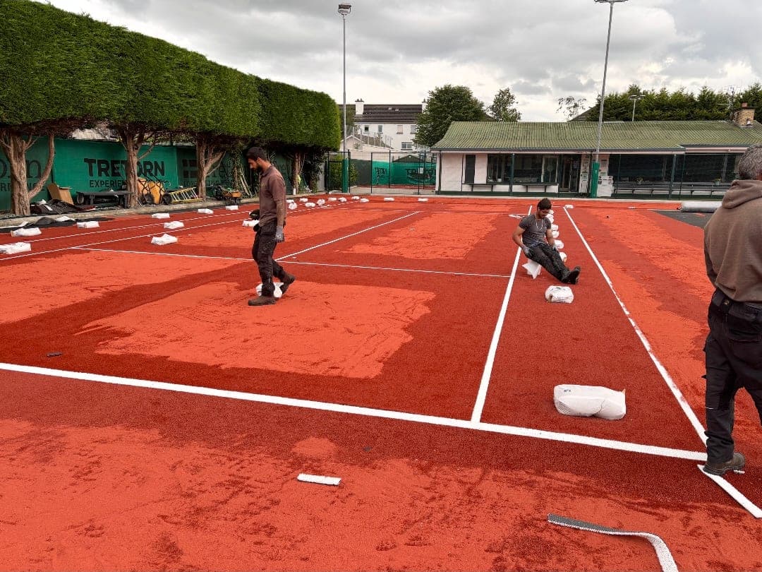 Crew spreading infill from bags across a newly laid red clay court at a tennis club
