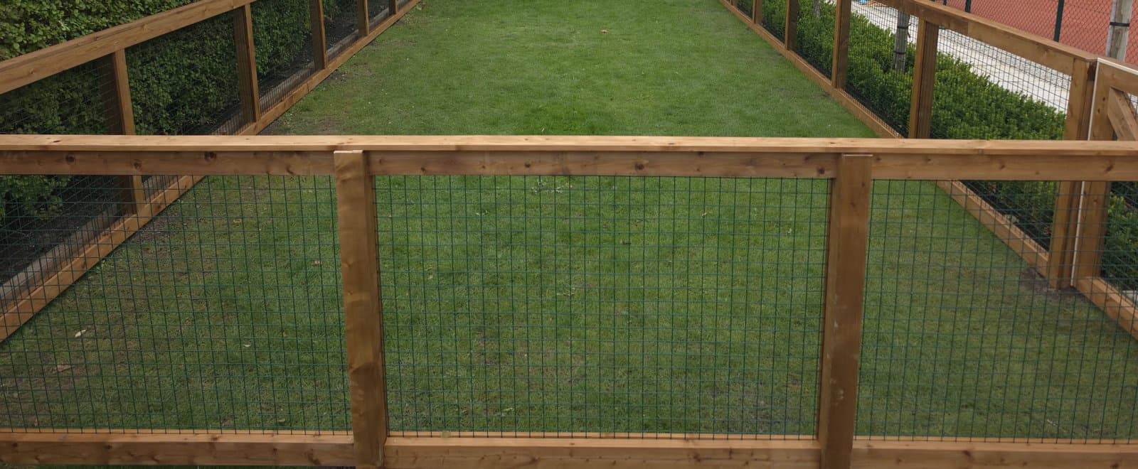 Timber post-and-rail fence with black mesh panels enclosing a long strip of lawn