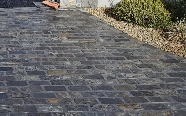 Rough-cut stone setts, damp after washing, beside a gravel bed with low shrubs