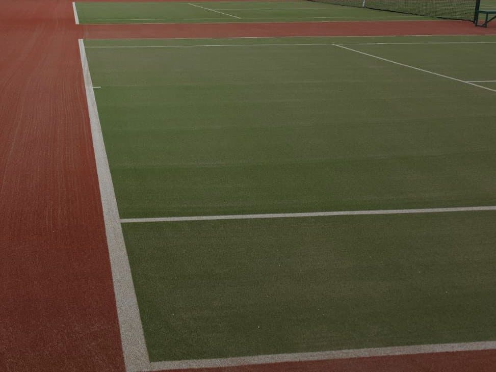 A green synthetic tennis court with red surrounds and white lines