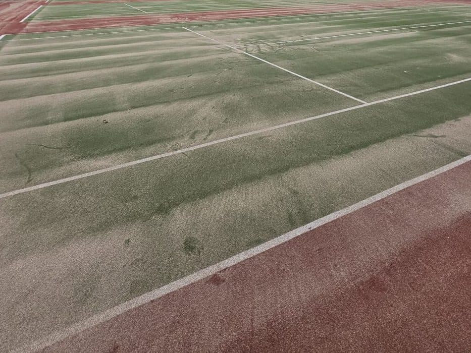 Sand infill brushed across a green synthetic tennis court, with brush marks over the surface