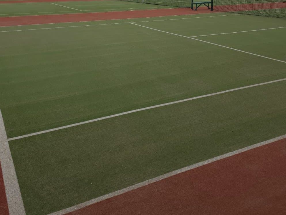 Green synthetic tennis courts with red surrounds, white lines and nets
